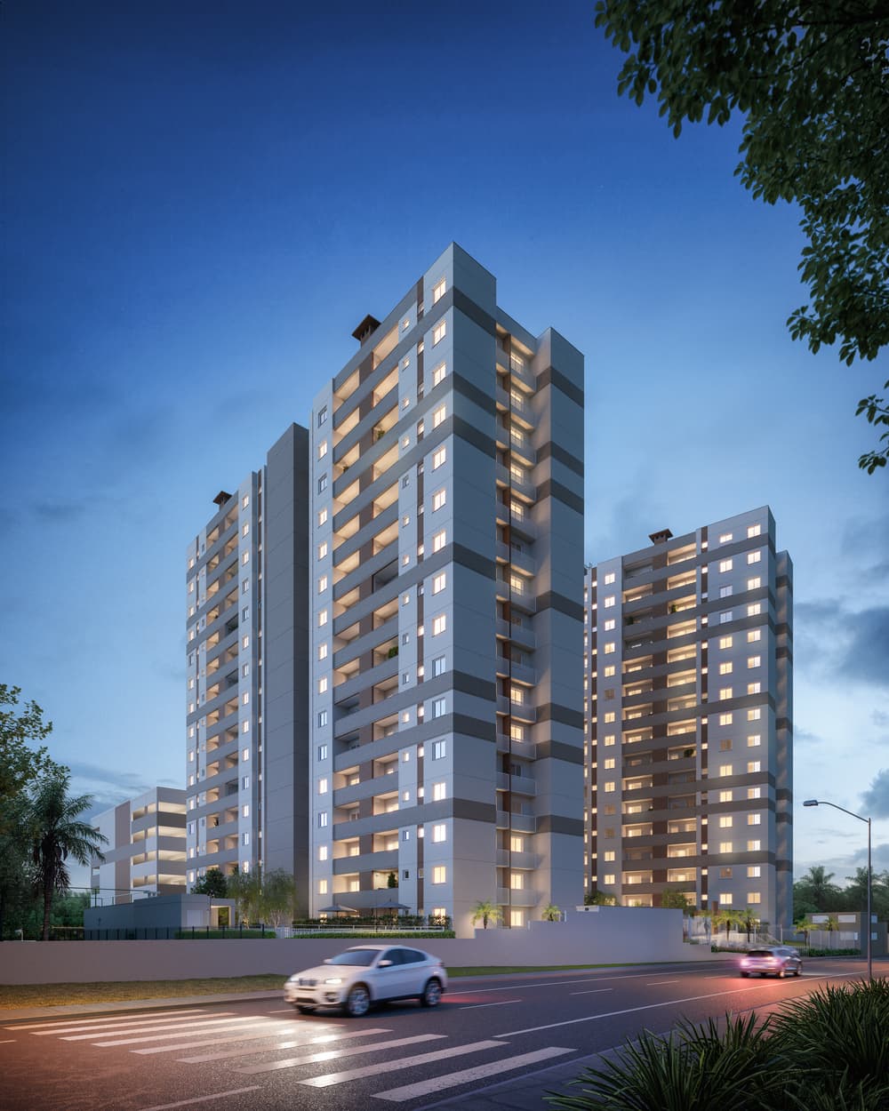 Fachada noturna de condomínio residencial com torres altas e iluminação nas janelas.